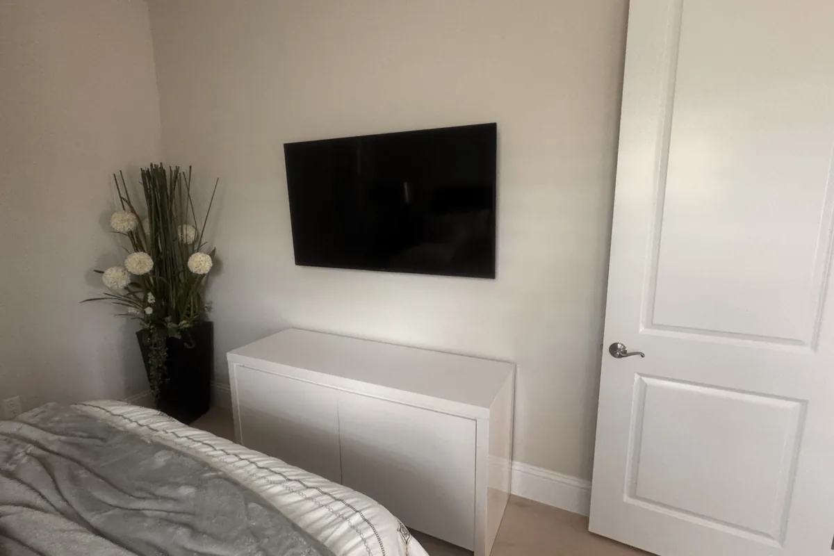 Clean bedroom TV mounting above white cabinet with plant decor